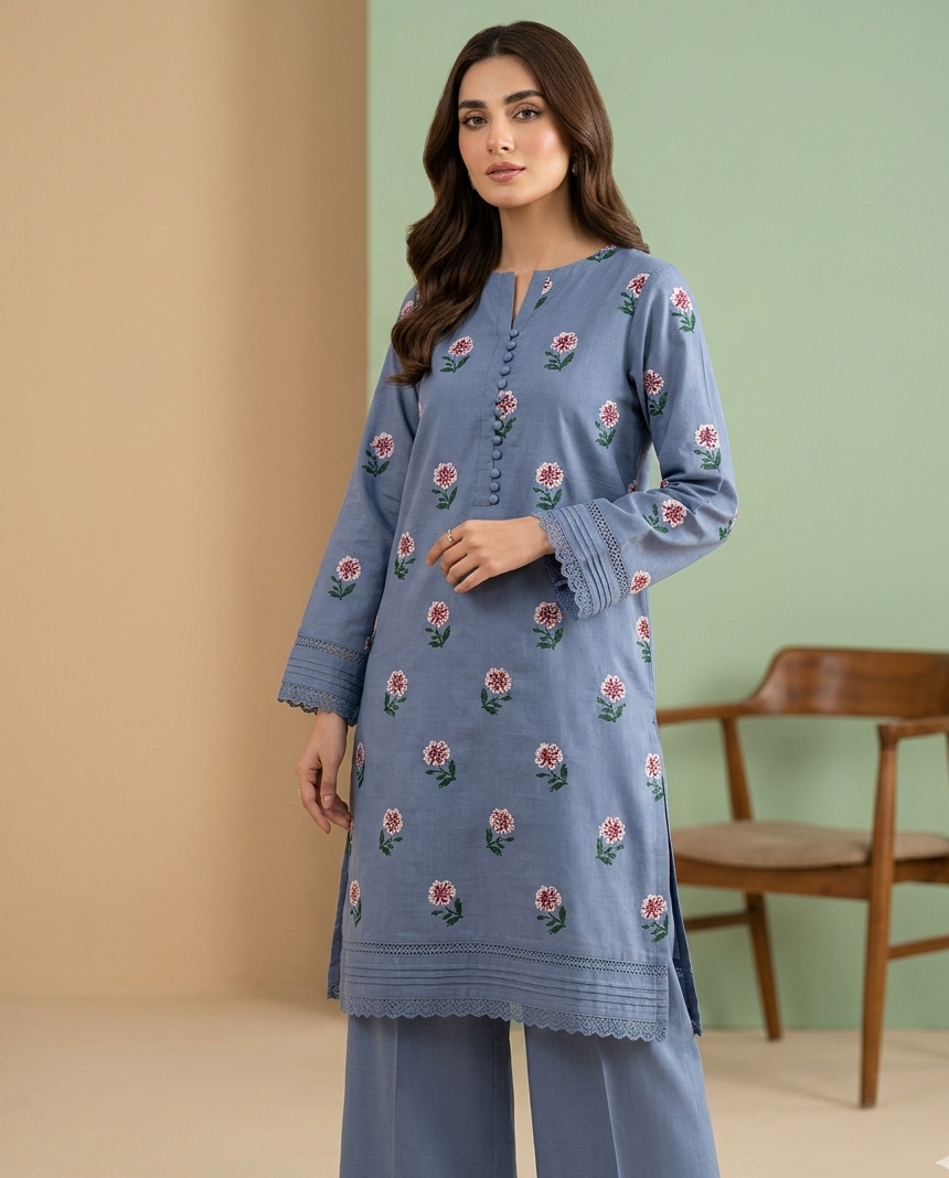 Woman wearing a blue embroidered outfit standing against a green wall with a wooden chair.