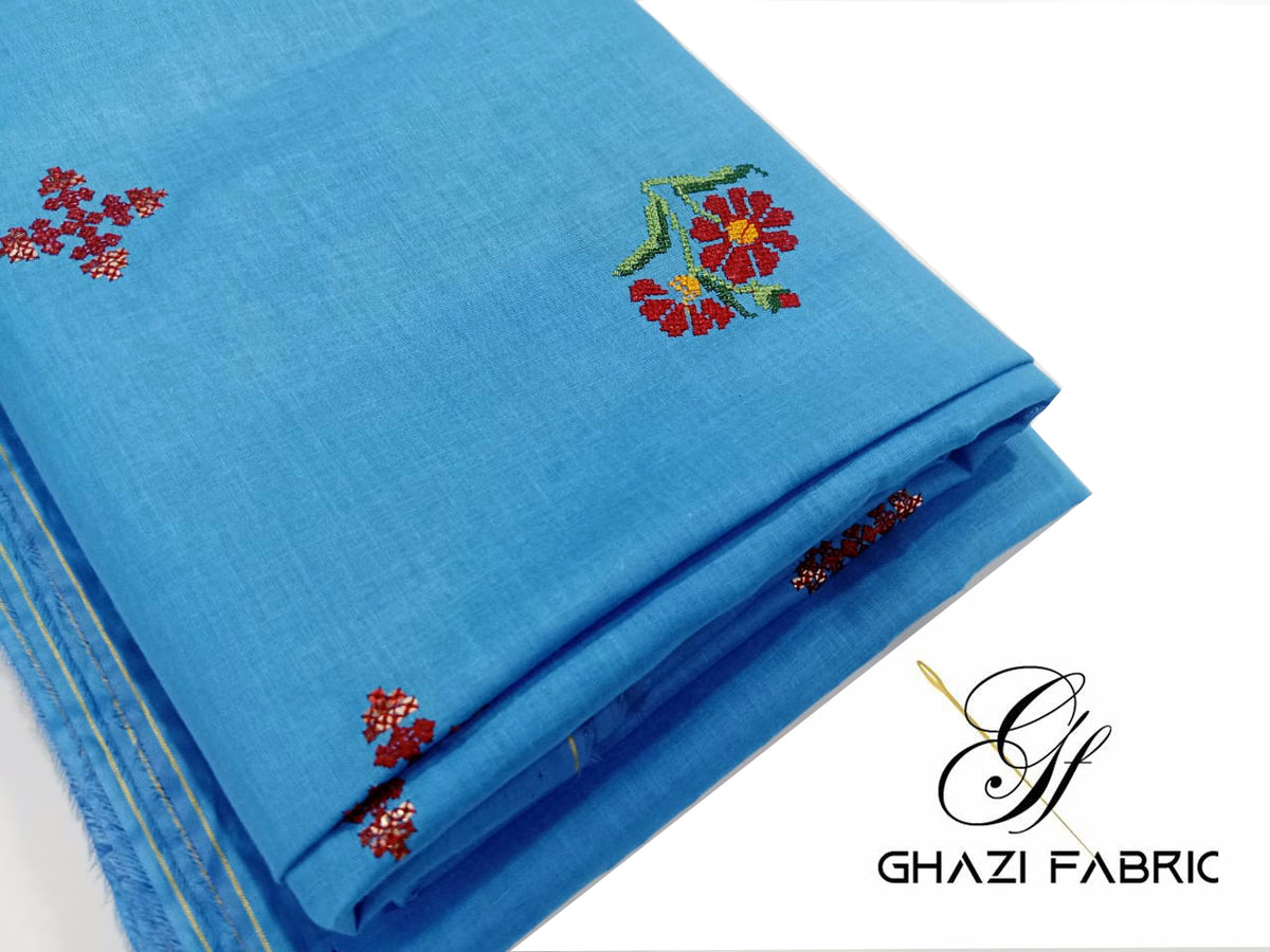 Blue fabric with floral embroidery and Ghazi Fabric logo.
