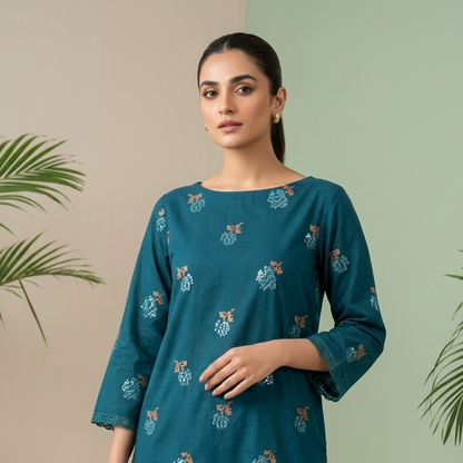 Woman wearing a teal embroidered outfit with a minimal background