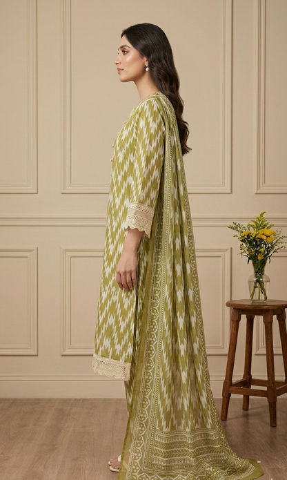 Woman in a green and white patterned outfit standing in a room with wooden flooring and a beige wall.