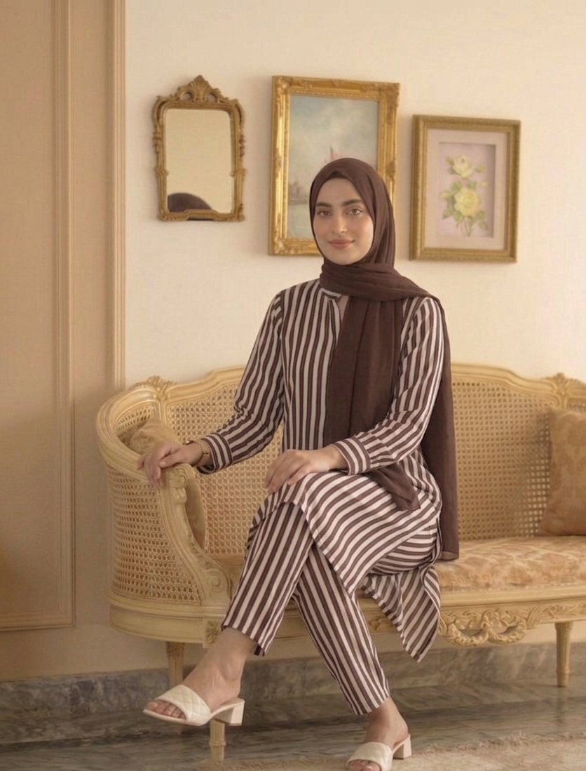 Woman in a striped outfit sitting on a vintage sofa in a room with framed pictures on the wall.