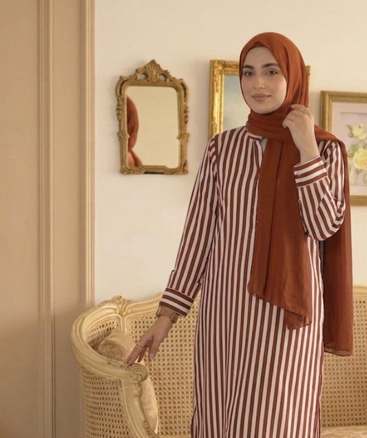 Woman in a striped outfit with a hijab standing in an elegant room.