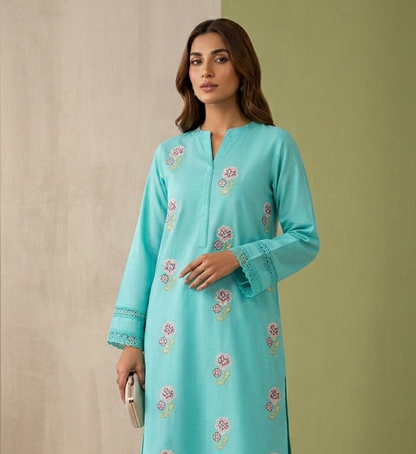 Woman wearing a turquoise embroidered outfit against a neutral background