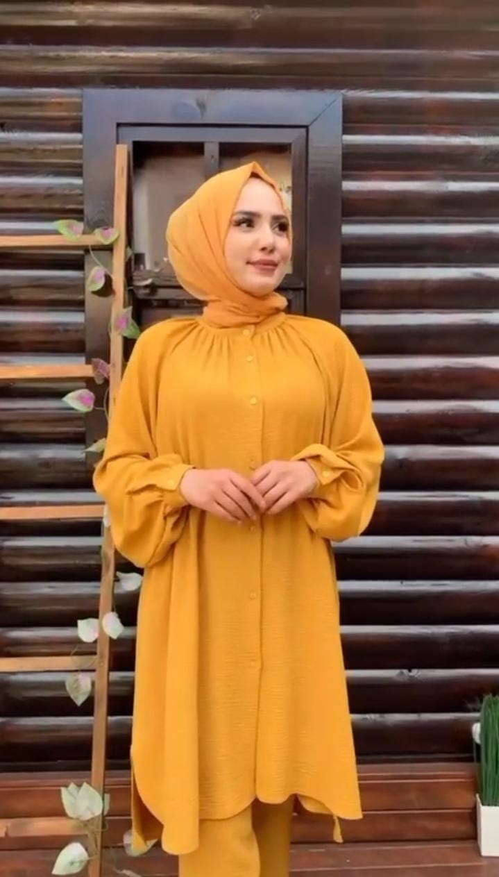 Woman wearing a mustard yellow outfit with a matching hijab against a wooden background
