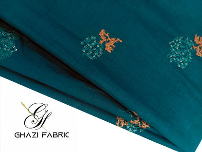 Teal fabric with gold embroidery, branded 'Ghazi Fabrics'.