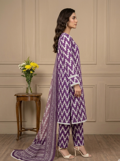 Woman in a purple and white patterned outfit standing in a room with a wooden table and flowers.